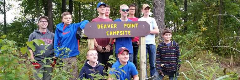 boy scouts pose with a campsite sign