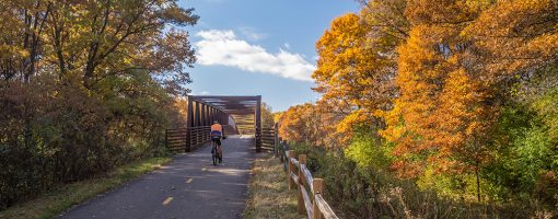 Bicyclist on paved trail approaching a bridge