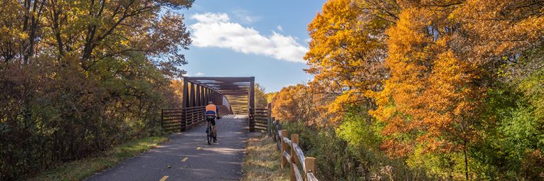 Bicyclist on paved trail approaching a bridge