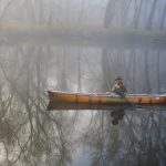 Man canoeing through misty river