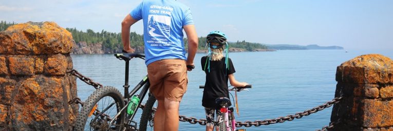 Father and daughter look over lake Superior with bikes