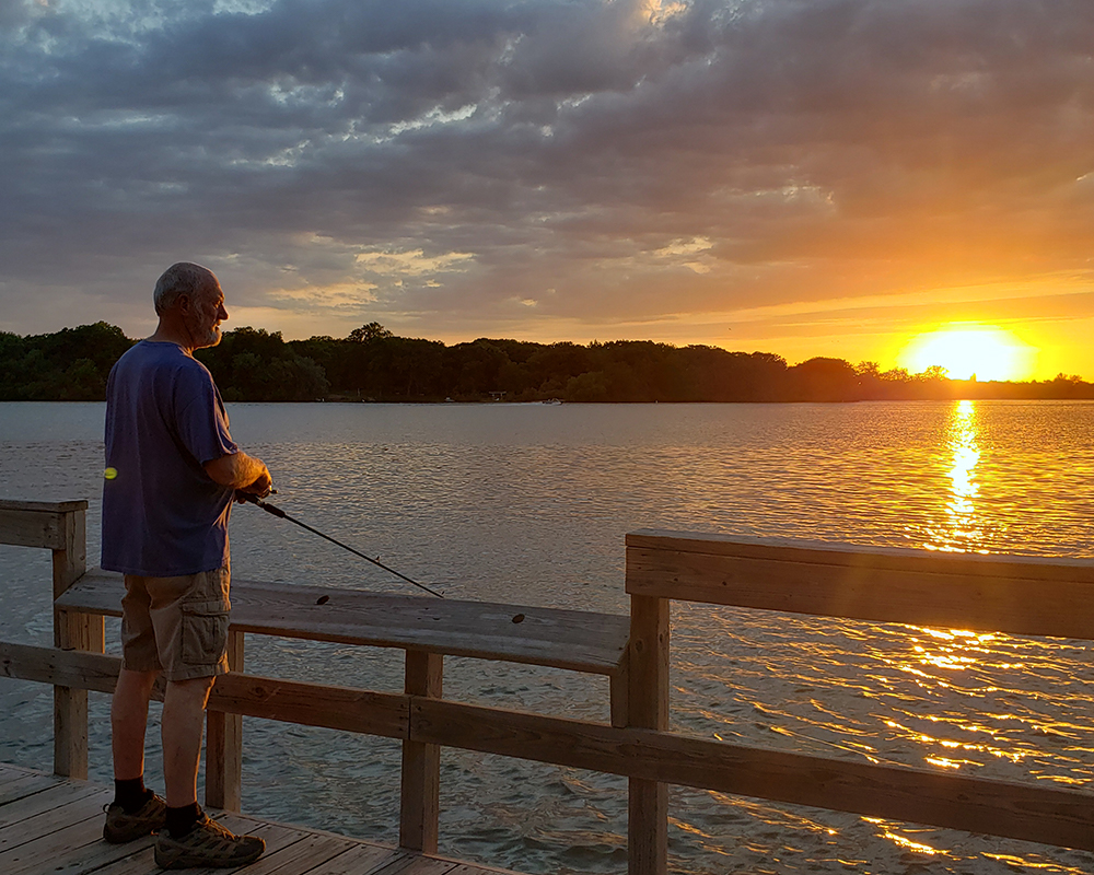 Older man fishing on pier at sunset