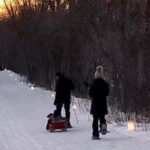 Two people walking on snowy trail lit by candles