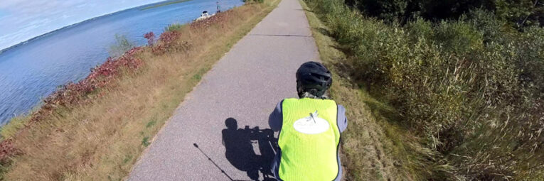 Person with bright yellow vest riding a bike on a trail with Lake Superior on their left