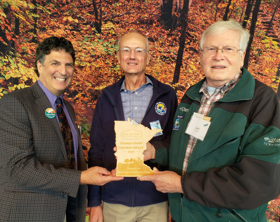 Three men holding a wooden award