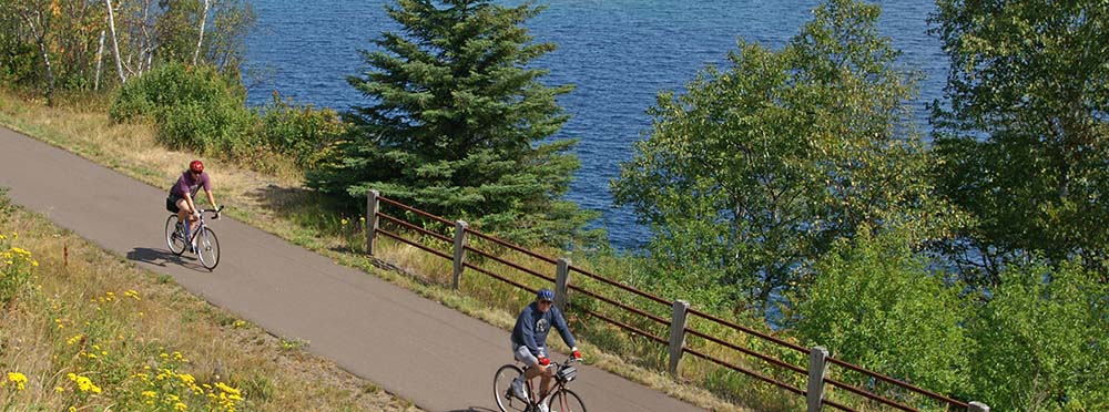 two bicyclists on a paved trail next to a lake