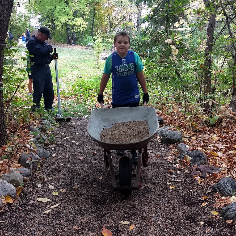 kid moves wheelbarrow with gravel for trails