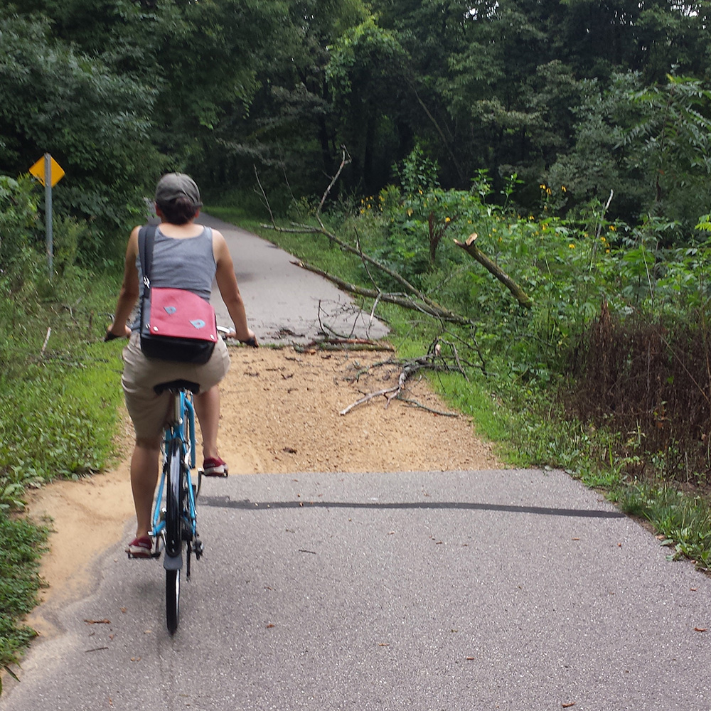 Woman bicyling on paved trail with a section of pavement missing