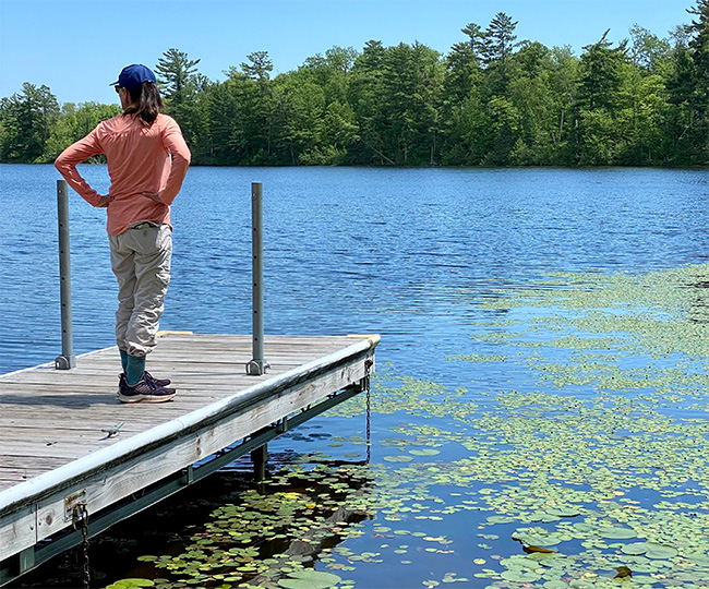 Woman standing on dock overlooking a pristine lake with lily pads