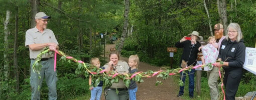 Members of the Friends of Tettegouche hold a ribbon intertwined with leaves while the assistant park manager prepares to cut it.