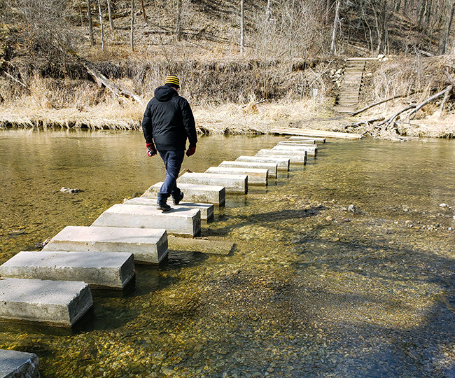Man crossing river on bridge made of concrete blocks