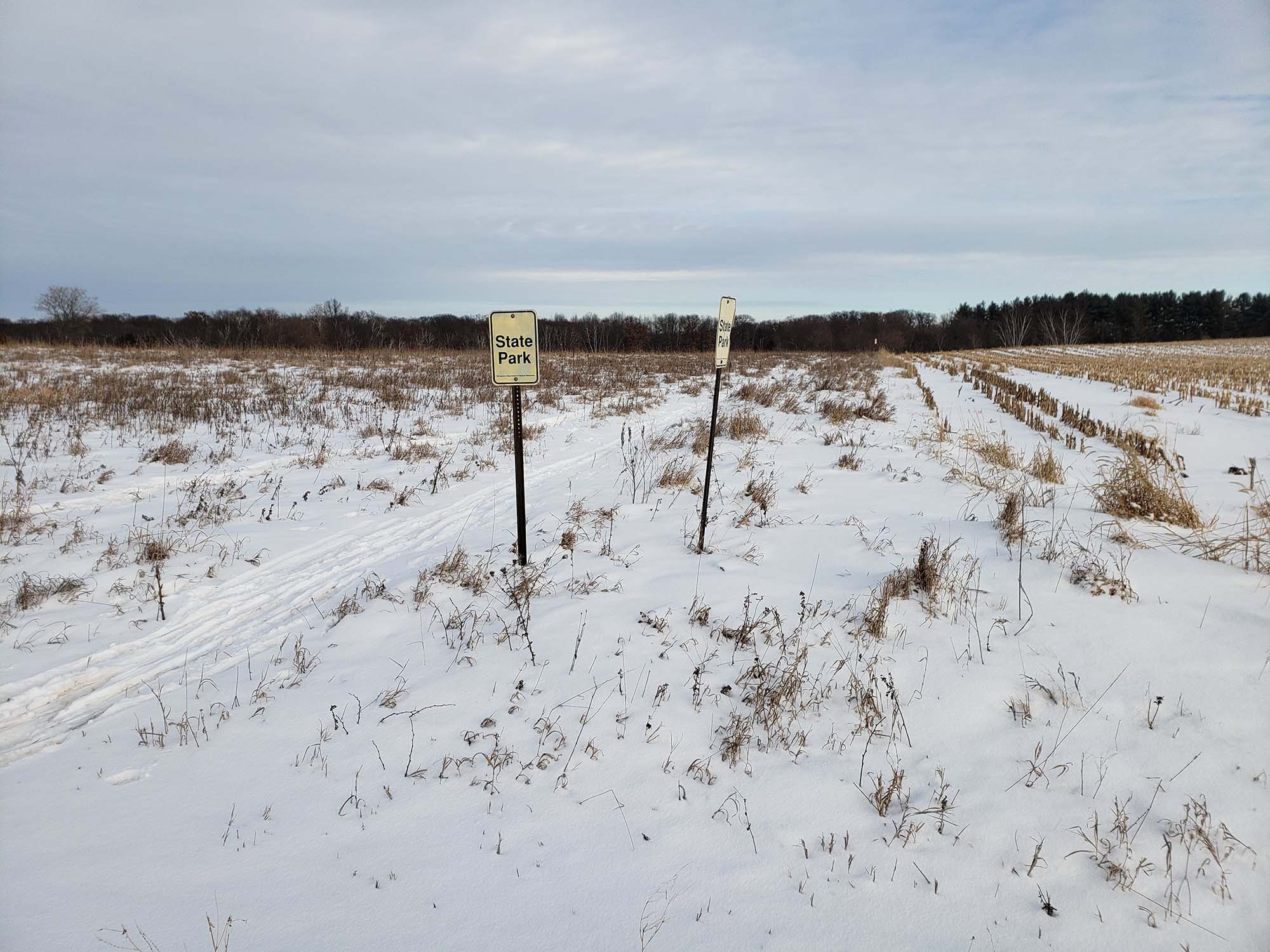 Snowy field with signs that mark border of the state park