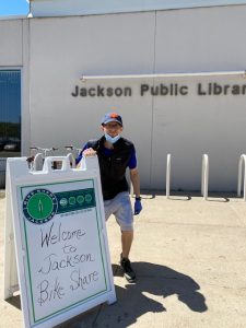 person in front of library stands next to sign that says "Welcome to Jackson Bike Share"